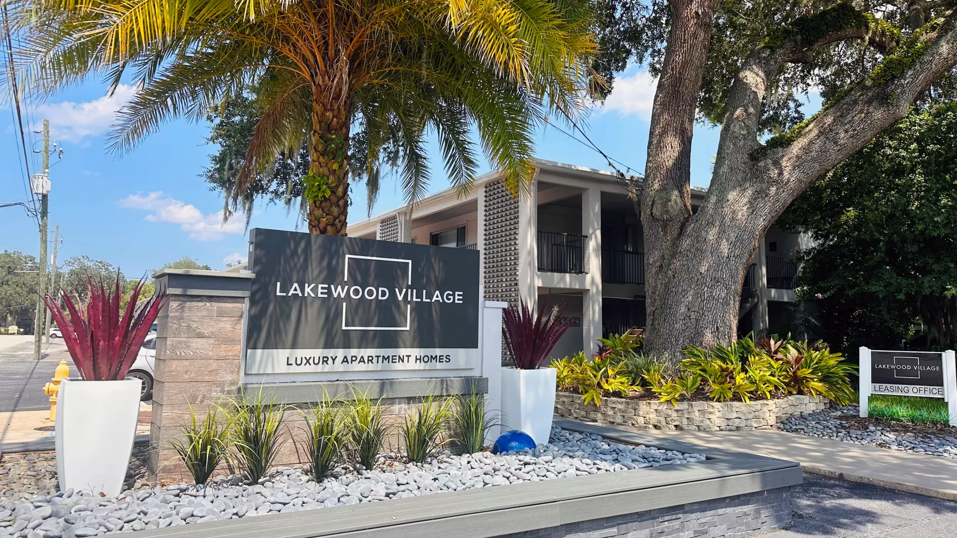 A prominent monument sign at the front entrance adorned with landscaped river rocks and large white planters creating a bold and inviting greeting to the community.