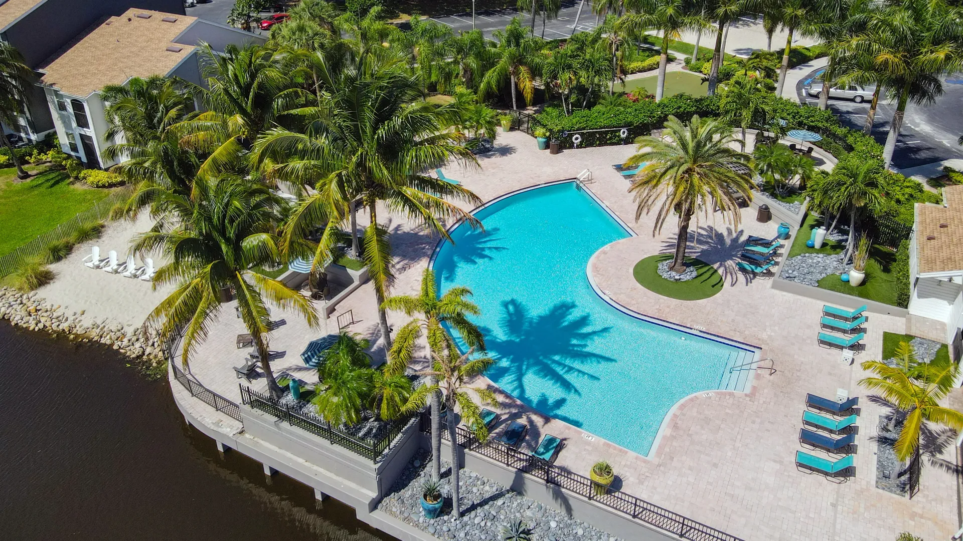 A picturesque aerial view highlighting the vast pool deck, vibrant palm trees, and tranquil lakefront vistas, creating an inviting setting for pure waterside relaxation amidst breathtaking natural beauty.