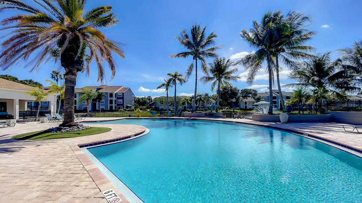 Sparkling pool waters glisten beneath cascading palm trees, creating topical vibes, inviting perpetual summer feels and year-round leisure in this serene and tranquil poolside setting with lake views in the distance.