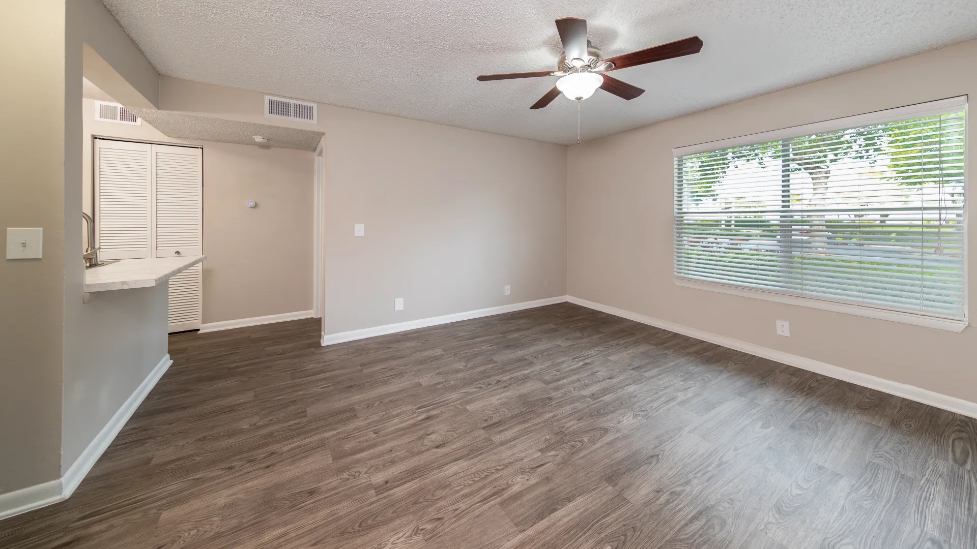 A breakfast bar cutout, a large countertop ledge from the kitchen, opens into the expansive living room with spacious wood-style floors and a massive window for optimal lighting.
