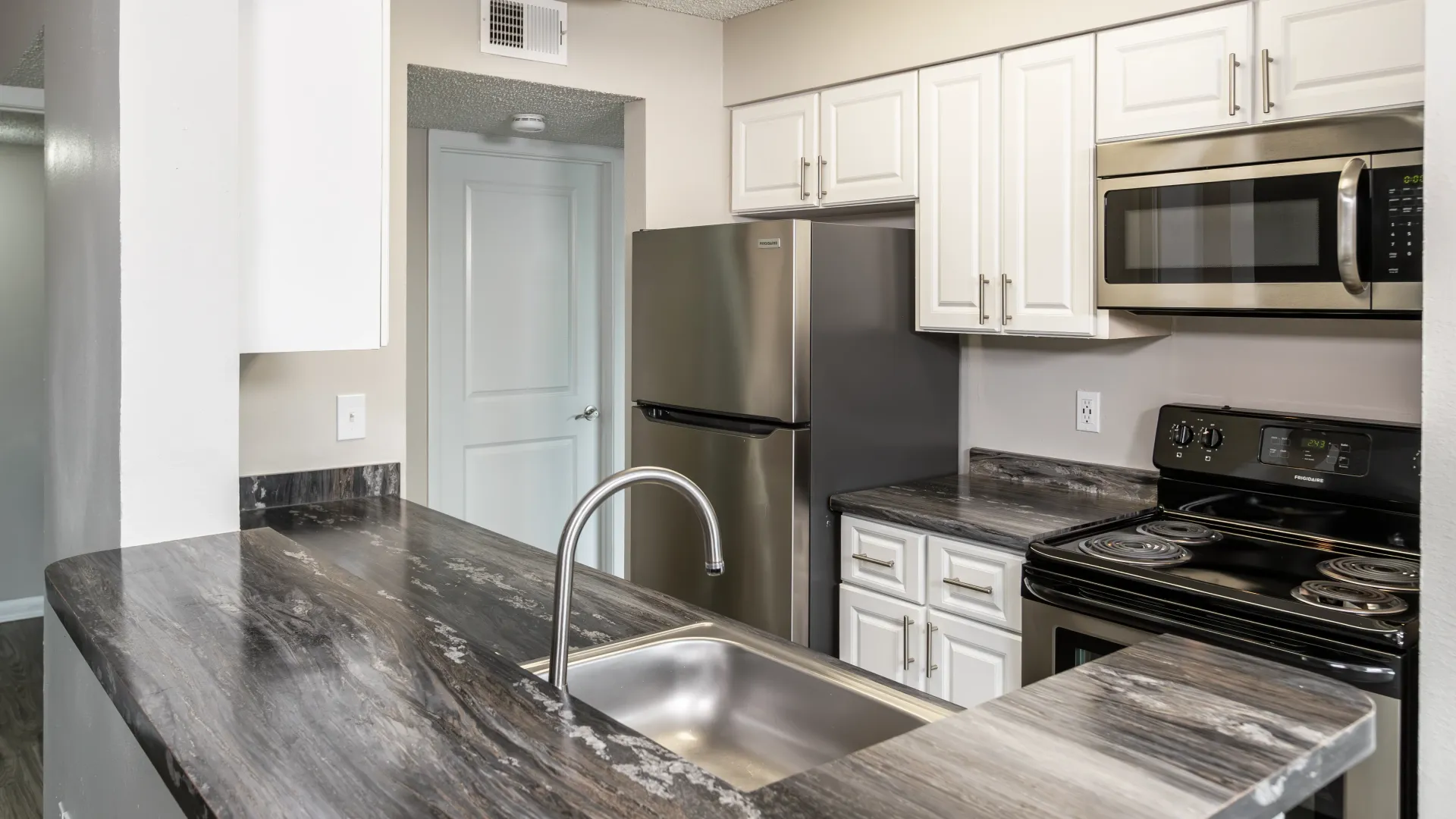 Galley-style kitchen featuring a breakfast bar, gleaming stainless-steel appliances, white cabinetry, and contemporary black fusion granite-inspired countertops.