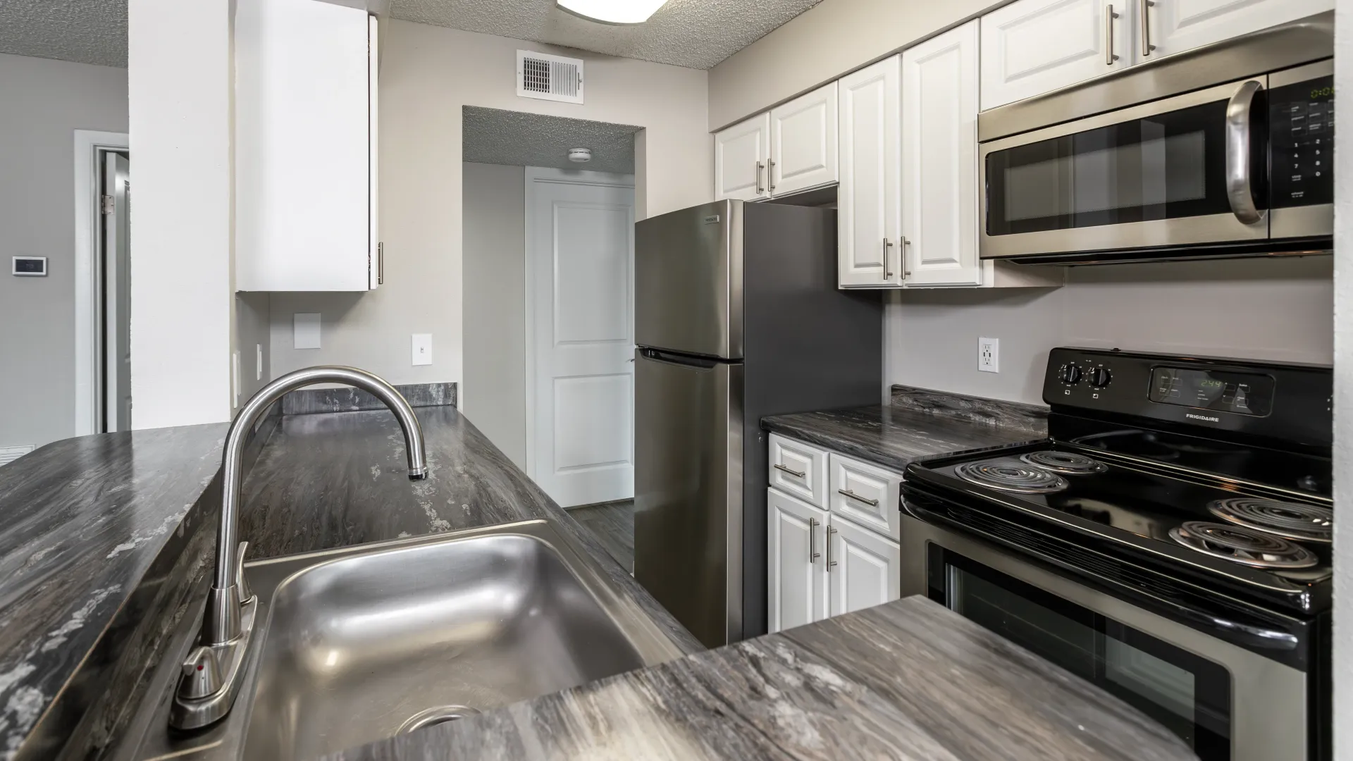A kitchen adorned with gleaming stainless-steel appliances, ample upper and lower cabinetry, and contemporary black fusion granite-inspired countertops. 