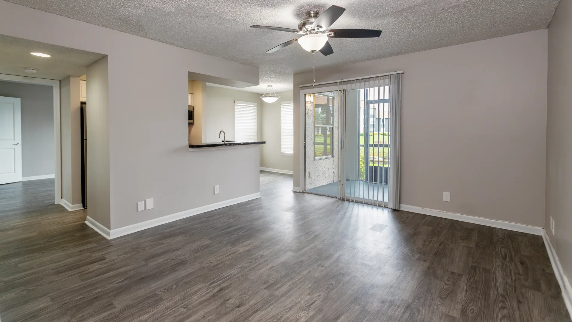 A seamlessly connected living space with expansive windows, open access between the kitchen, dining, and living areas, and sliding patio doors leading to the connected patio.