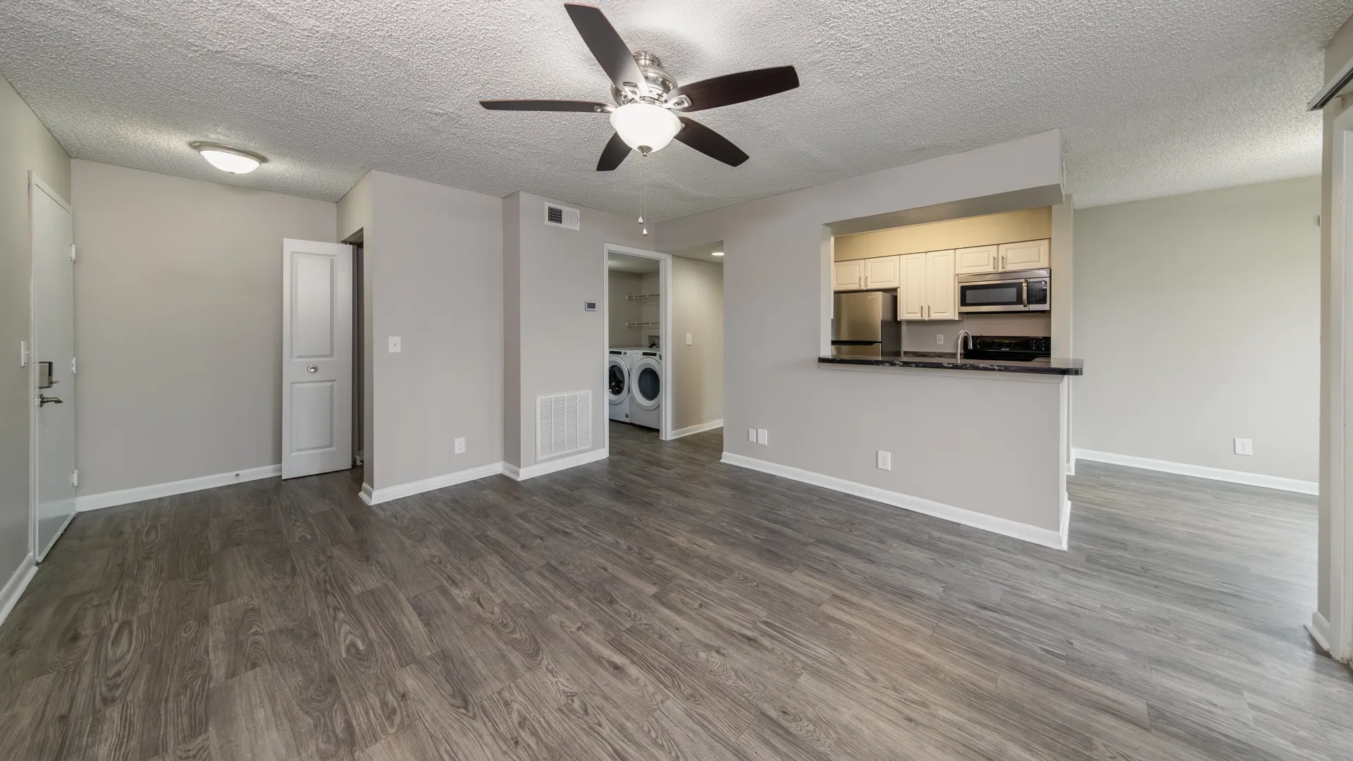 The expansive open-concept living room seamlessly merges with the kitchen, featuring wood-inspired floors, with a look into the massive laundry room with abundant storage.