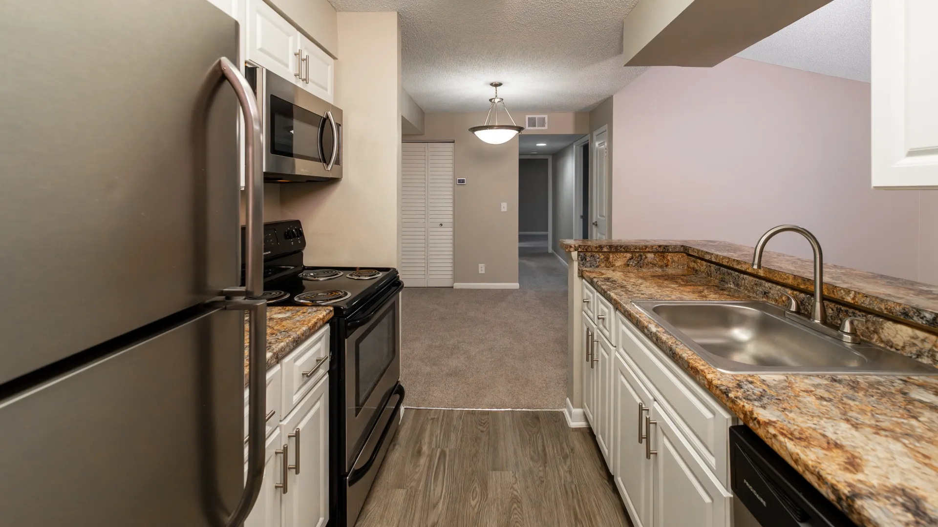 Chic kitchen displaying a cut-out breakfast bar, gleaming stainless-steel appliances, white cabinetry, and neutral palleted granite-inspired counters. 
