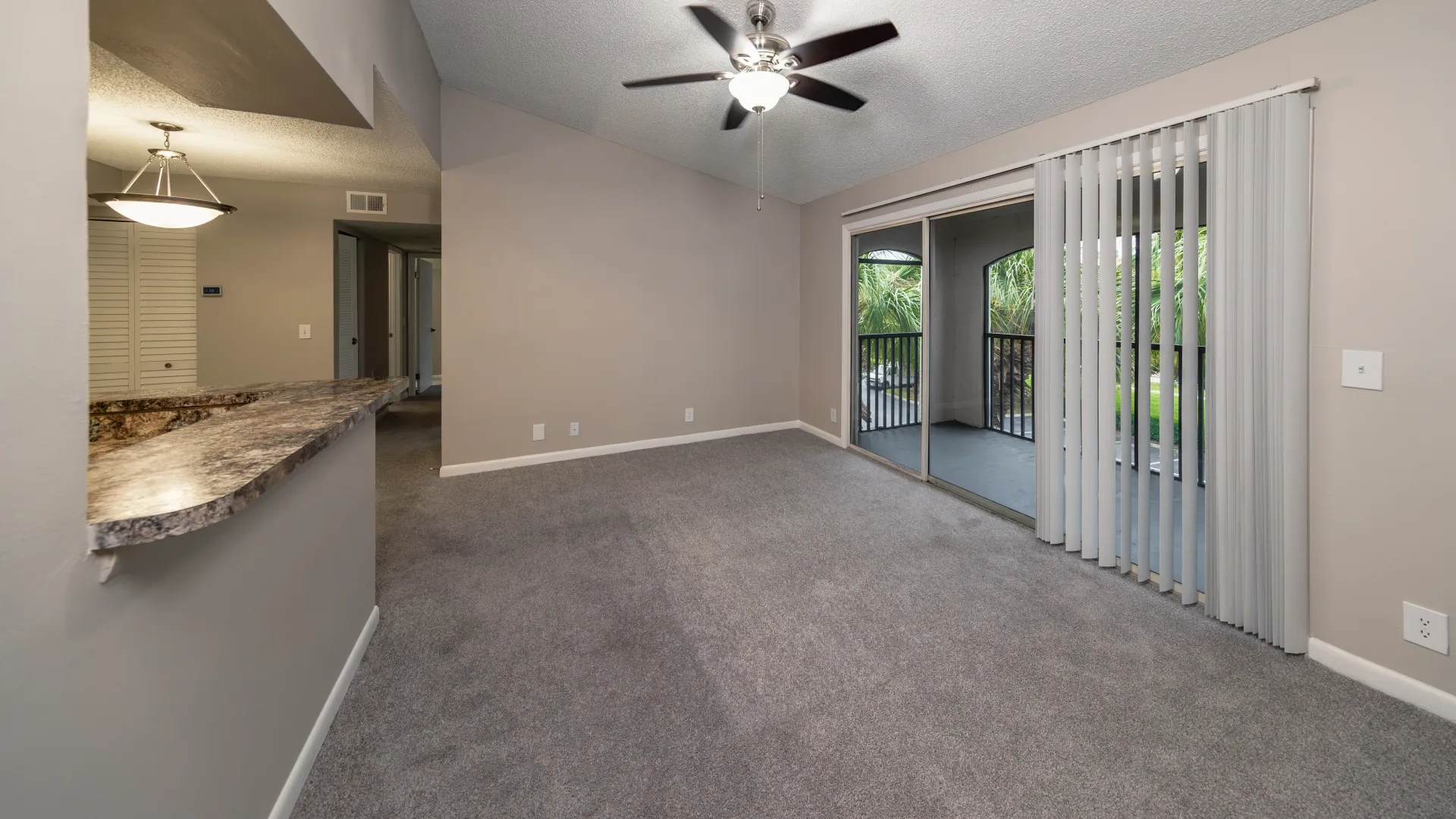 An open-concept living room with an inviting breakfast bar, lush carpeting, and expansive sliding patio doors revealing a vast, screened-in outdoor patio space. 