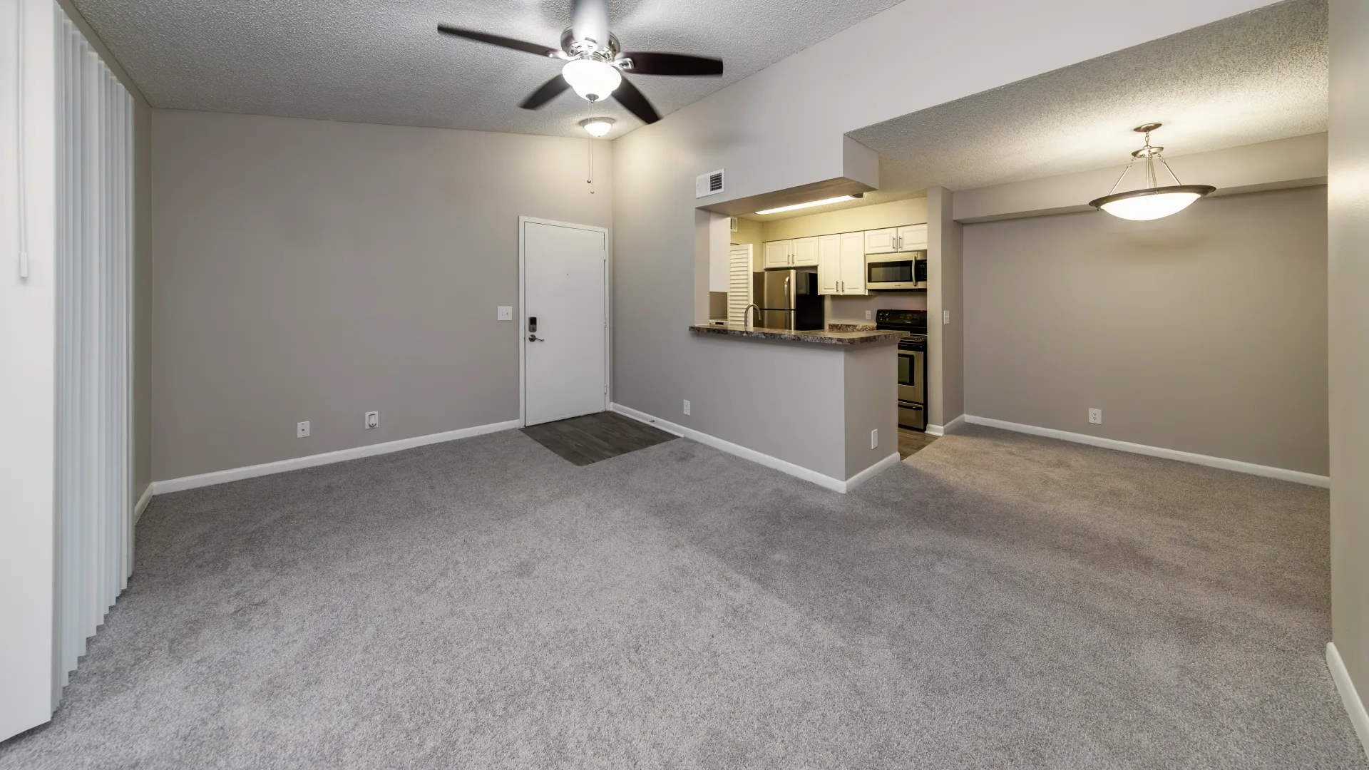 An open-concept living room, plush carpets, bright fan seamlessly transitions to the kitchen with a view across the breakfast bar into the dedicated dining space.