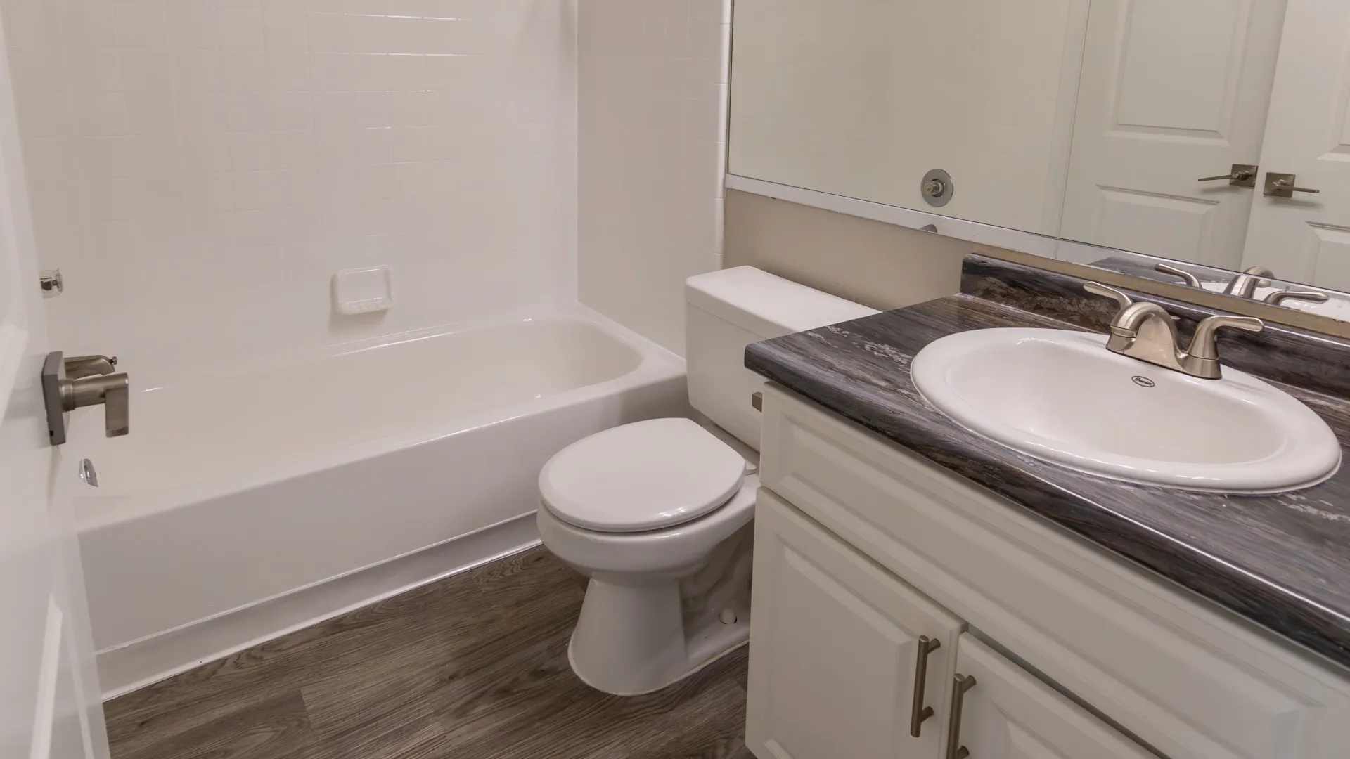 A well-lit bright bathroom featuring wood-style flooring, granite-style countertops, and a massive mirror, transforming your bath into a space of tranquility.