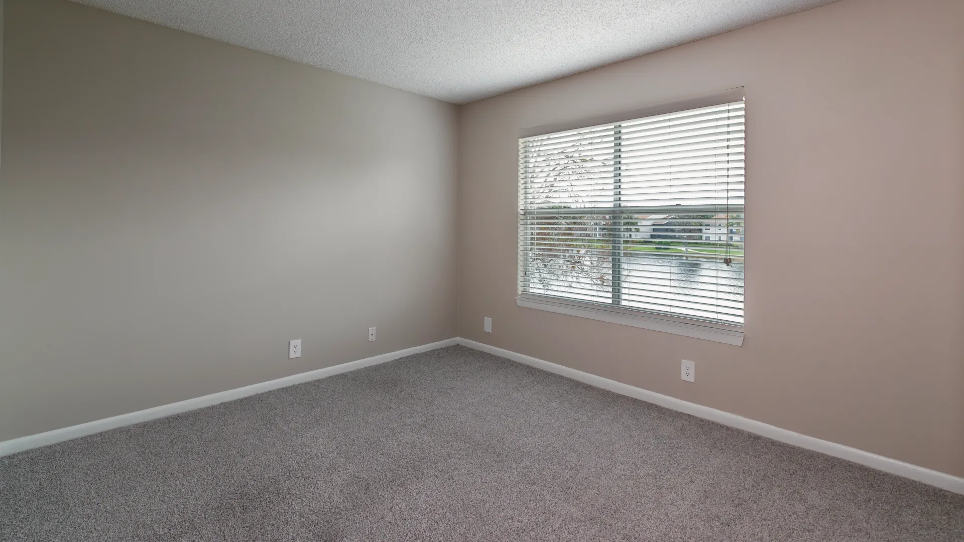 An extra-large Pacific Star bedroom flooded with brilliant lighting from large windows dressed in wood-style blinds, harmonizing with plush, neutral-colored carpeting.