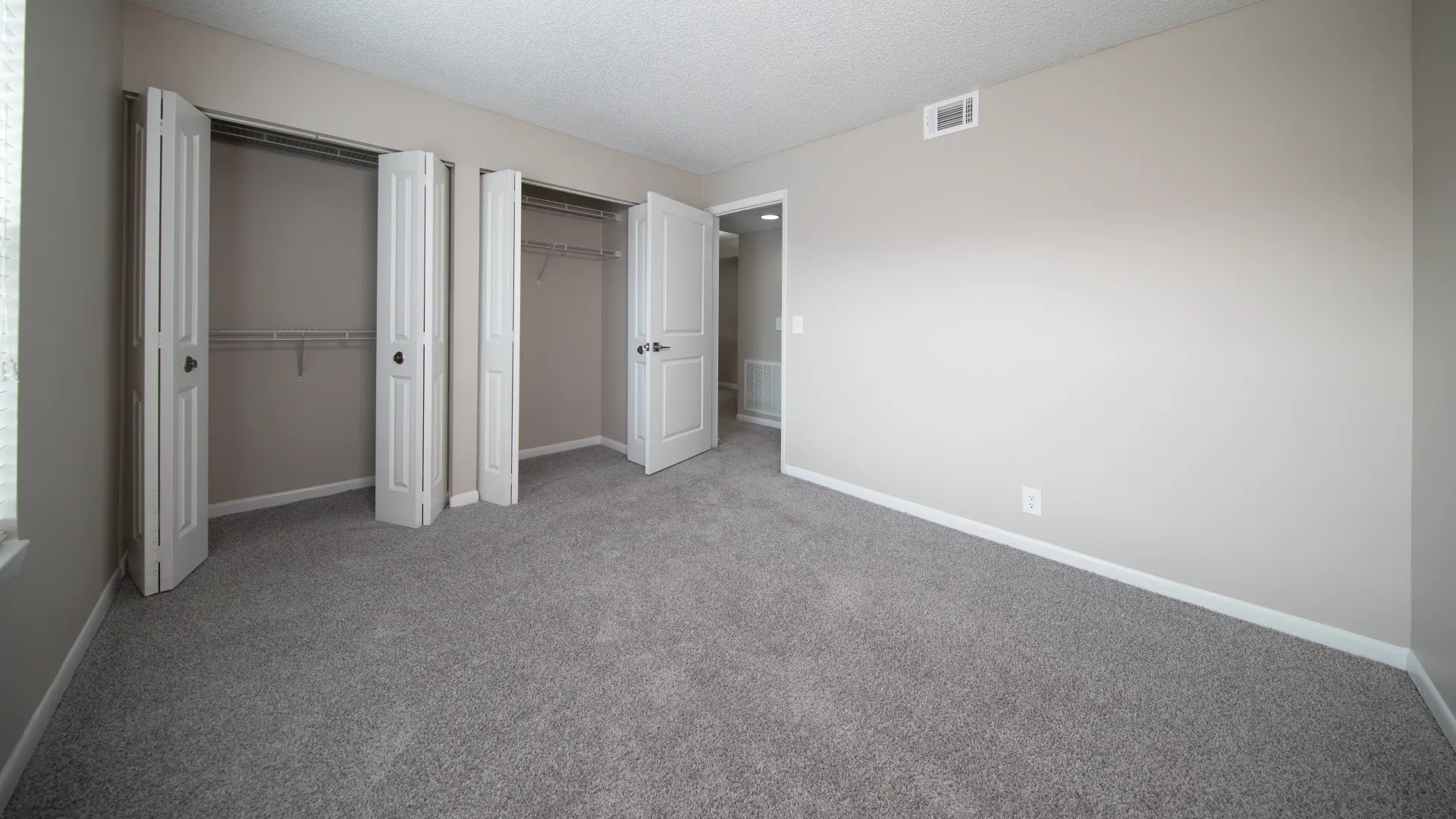 An extra spacious bedroom featuring soft carpeting and two closets, each boasting double bifold doors and expertly designed built-in shelving for unparalleled wardrobe luxury.