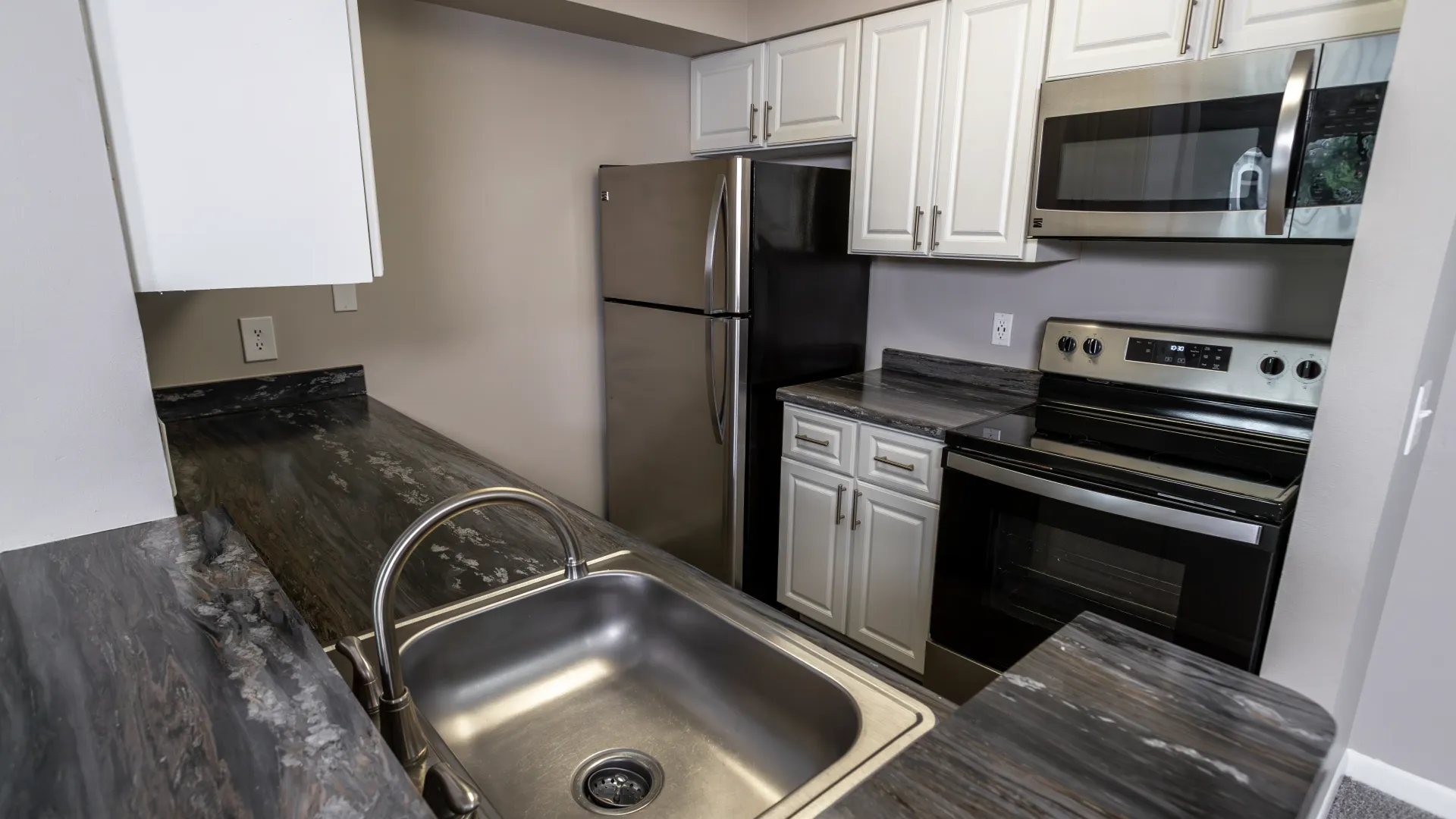 A galley-style kitchen showcasing gleaming refrigerator, microwave mounted over the stove, and abundant storage in stylish white cabinets.