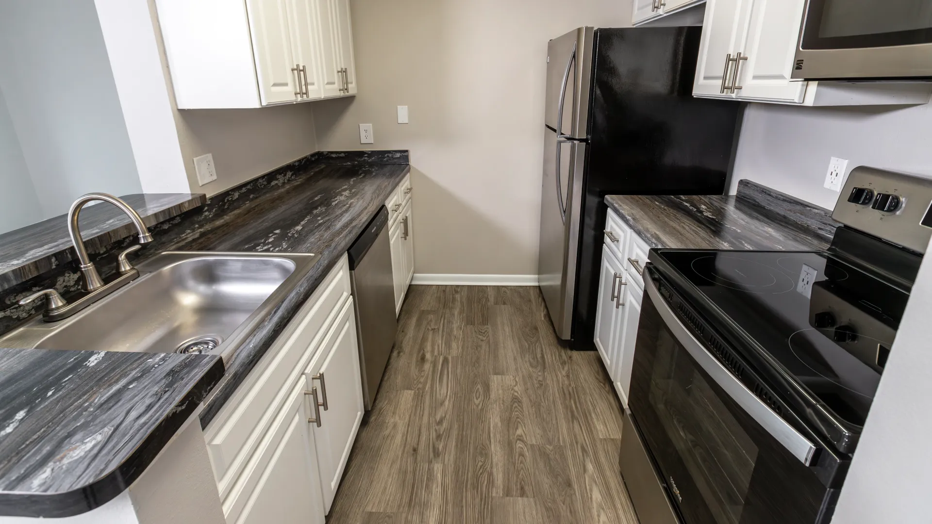 A kitchen with exquisite granite-style countertops, shimmering stainless-steel appliances, chic white cabinets for ample storage, and wood-styled flooring. 