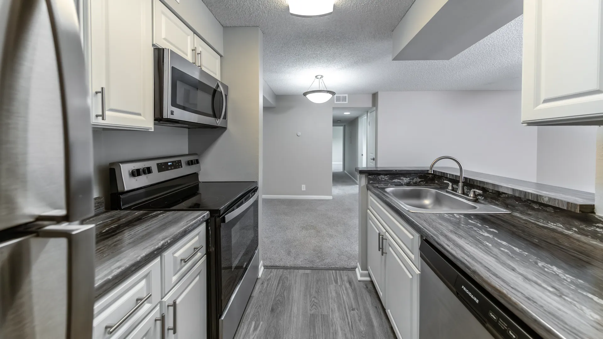 Shimmery stainless-steel refrigerator and mounted microwave over the stove with ample cabinetry, and sprawling black fusion granite countertops - complete with the added dimension of open views into dining and living areas. 