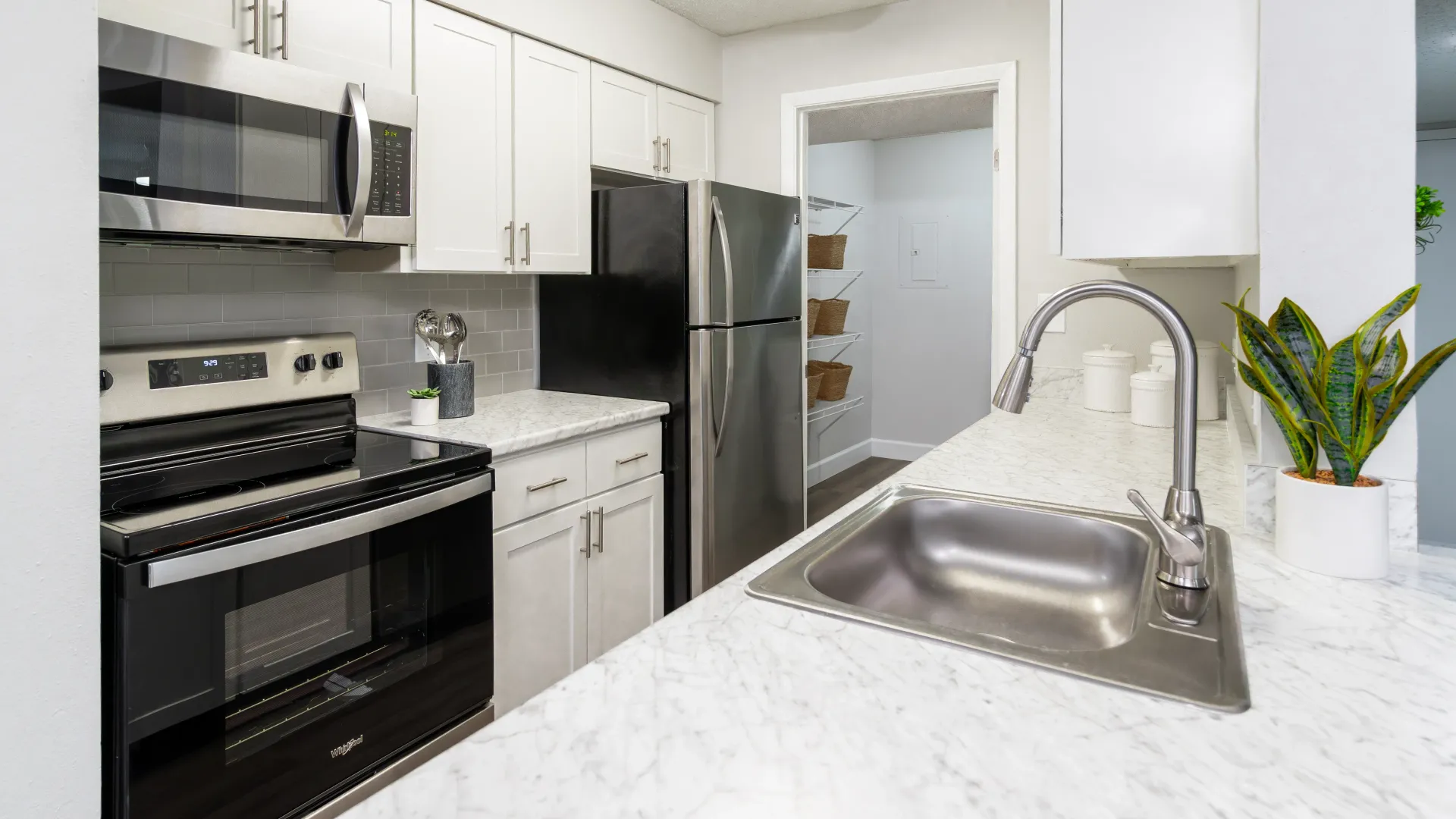 A view into a galley-style kitchen with a stainless-steel appliance package, robust storage options, and sparkling white countertops. 