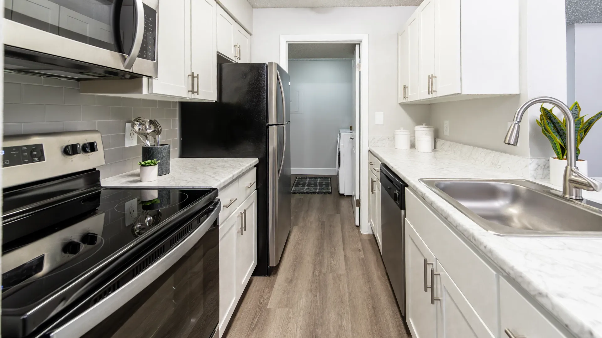 A view into a galley kitchen showcasing the elegant white Carrara countertops and abundant upper and lower white shaker cabinets. 