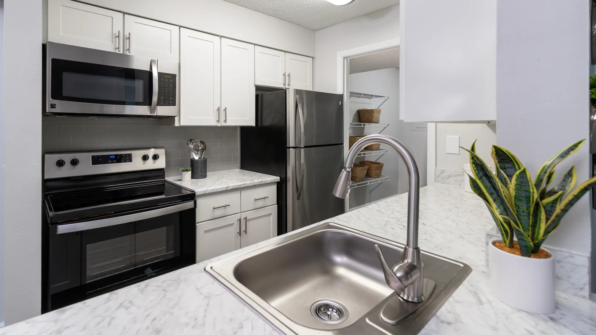 Polished Frigidaire appliances in a remodeled galley kitchen with a bonus pantry and modern finishes including a goose-neck faucet and timeless white shaker cabinets.