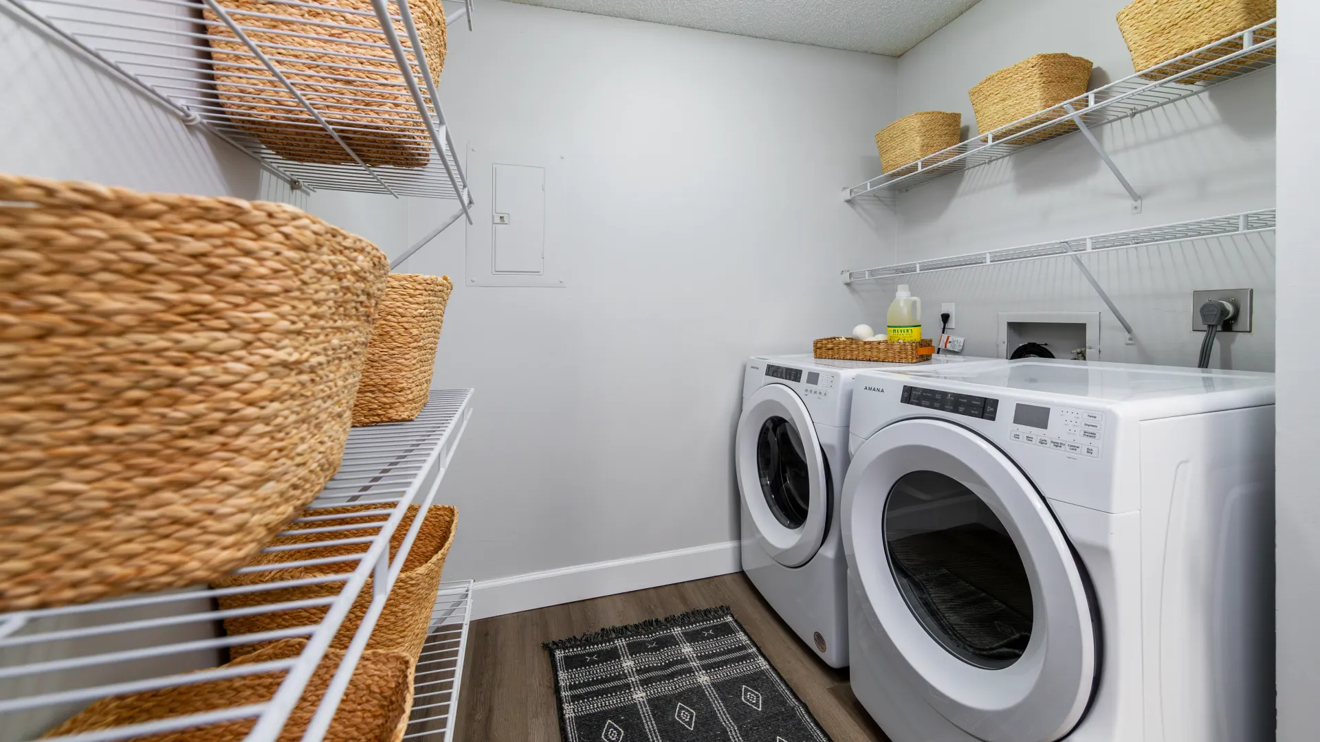 An exceptionally large laundry room with bonus pantry storage offered by customized open-wire shelving above and across from appliances. 