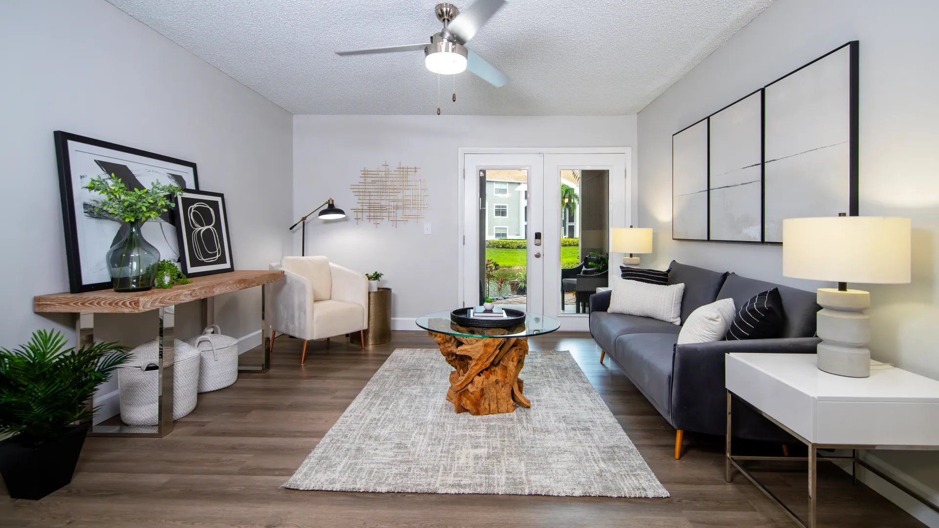 A lavish living space with wood-like flooring and a stylish fan with glass patio doors that leads to an adjoining lanai. 