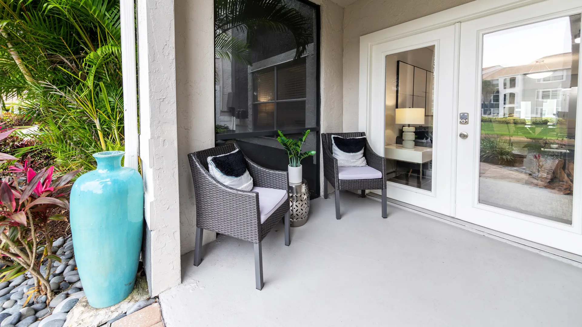 A spacious outdoor nook furnished with outdoor lounge chairs, an extension of the living room seen through the double glass doors. 