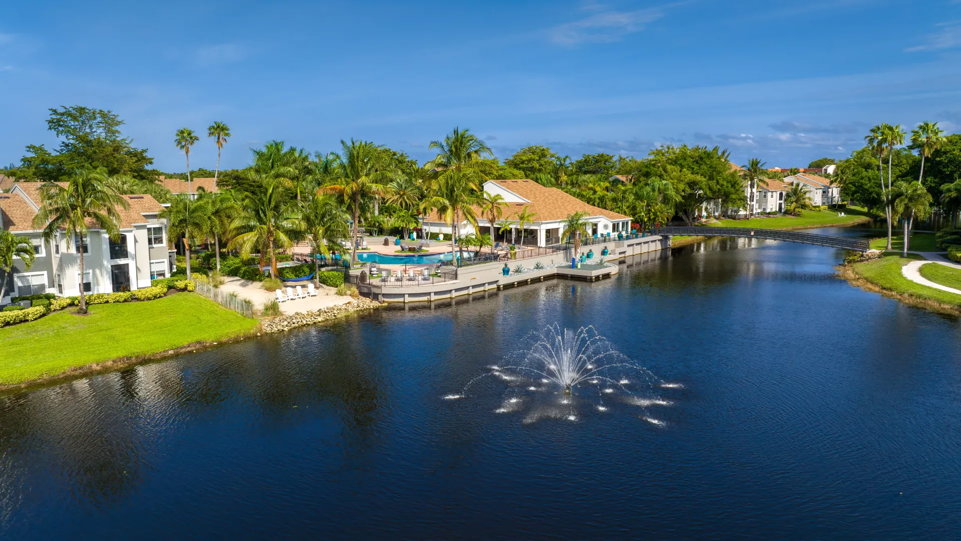 A picturesque aerial view showcases the vast pool deck, vibrant palm trees, and tranquil lakefront vistas, creating an inviting setting for pure waterside relaxation amidst breathtaking natural beauty.
