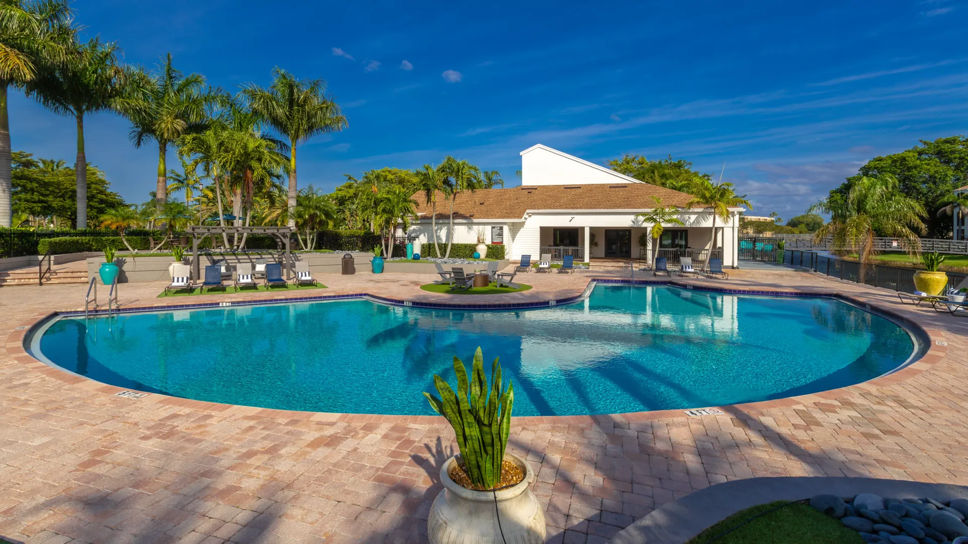 Sparkling pool waters glisten beneath cascading palm trees, creating tropical vibes, inviting perpetual summer feels and year-round leisure in this serene and tranquil poolside setting with lake views in the distance.