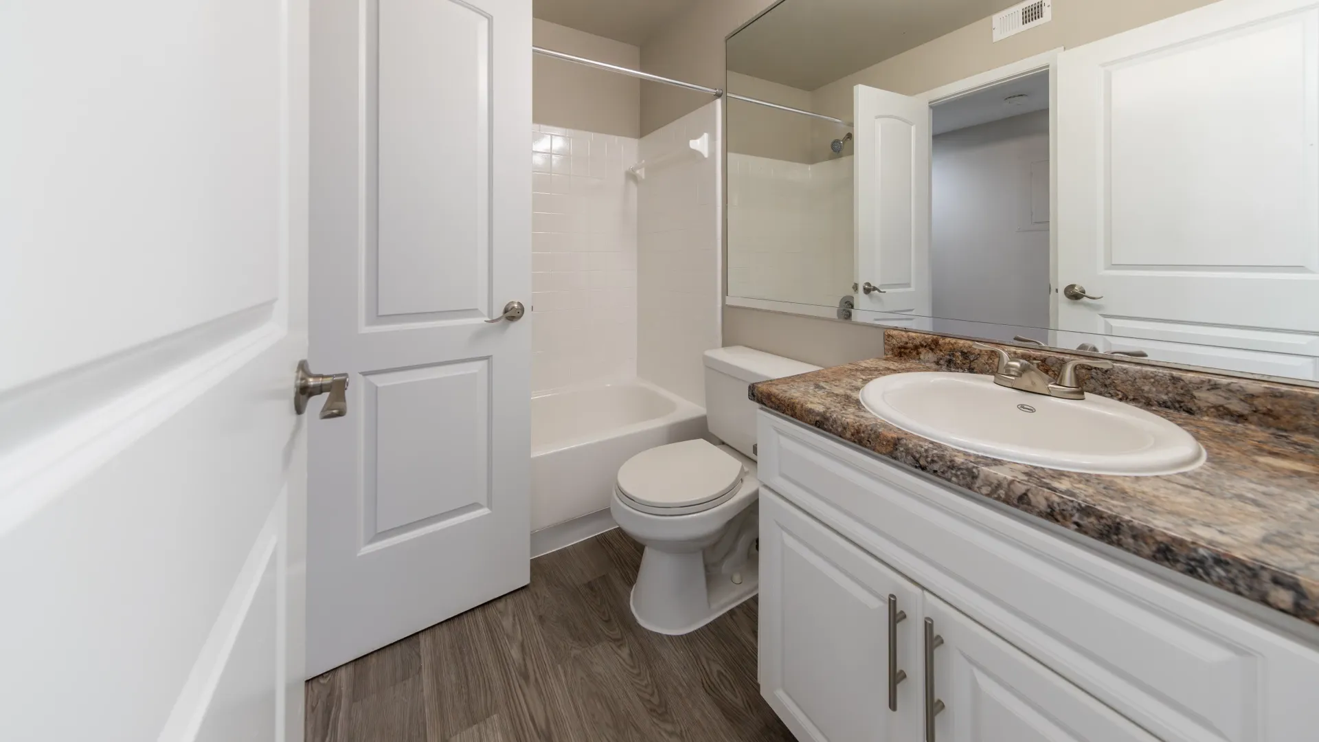 An illuminated vanity space featuring an expansive granite-inspired countertop, an enormous mirror, and ample cabinet storage below, creating a refined and well-lit haven in your master bathroom.