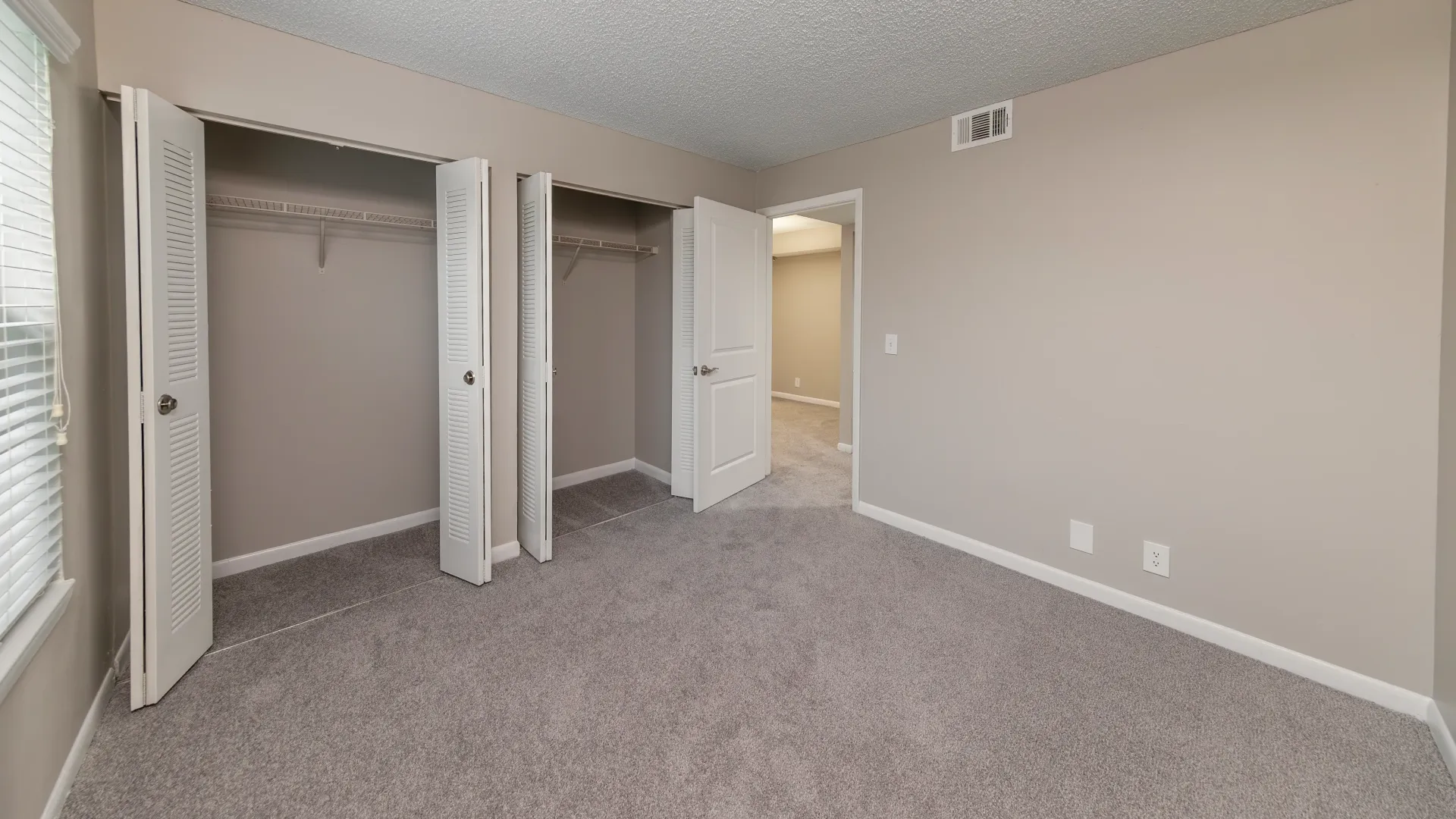 An extra spacious bedroom adorned with plush carpeting and two closets featuring double bifold doors with meticulously crafted built-in shelving for optimal organization.