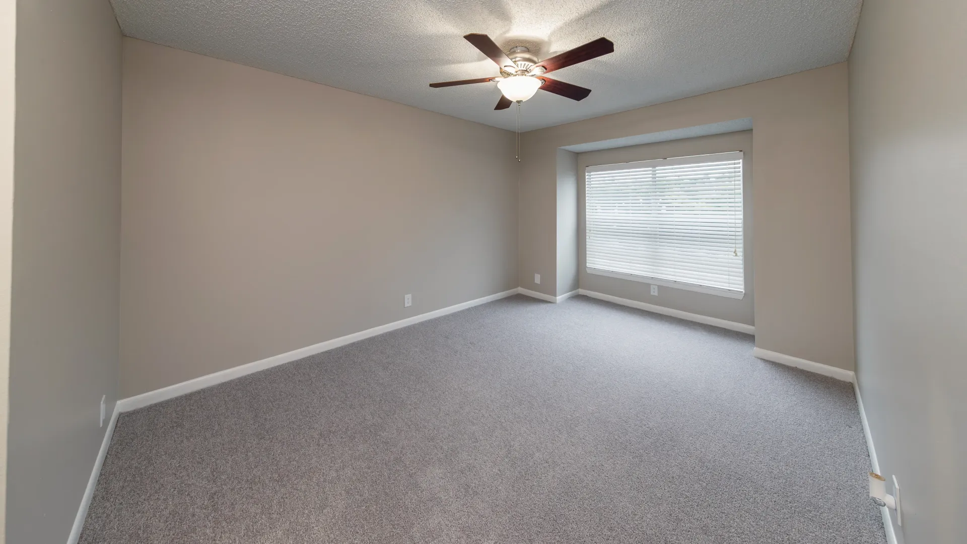 A huge master bedroom, featuring sumptuous plush carpet floors, a charming ceiling fan, and a broad window with privacy blinds, creating a retreat of pure comfort.