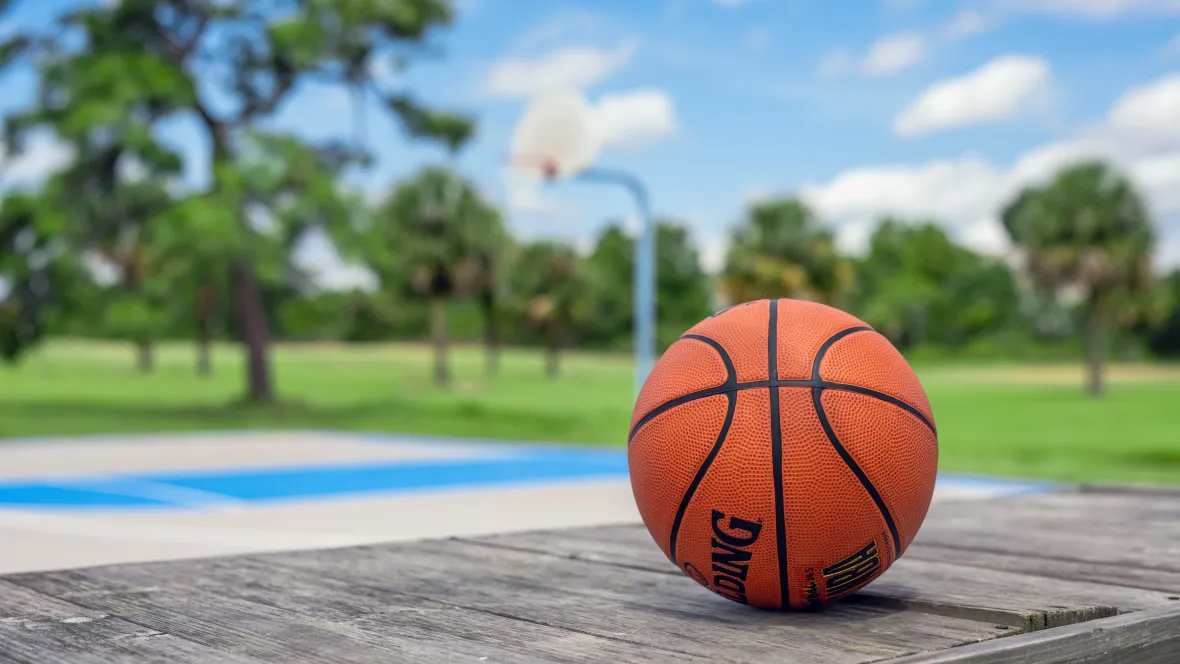 A basketball with a well-maintained court against the green landscape of the community creating the perfect outdoor backdrop of an active community. 