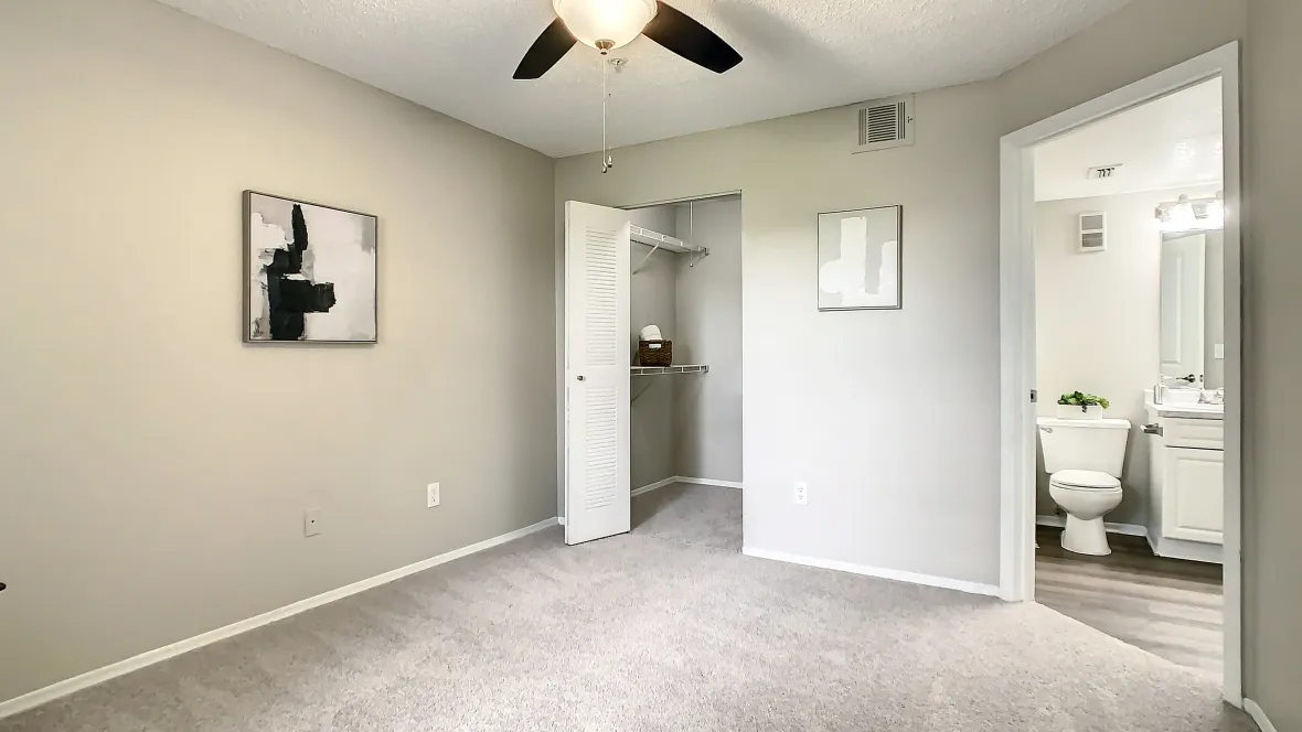 Guest Bedroom with plush carpet, a walk-in closet with shelving, and an adjoining private bathroom. 