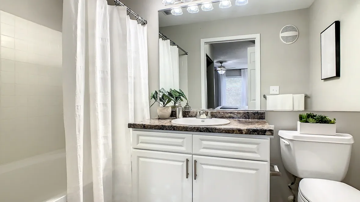 A serene bathroom space boasting roomy countertops, ample overhead vanity lighting, an extensive mirror, and a sophisticated white tiled surround shower/tub combo.