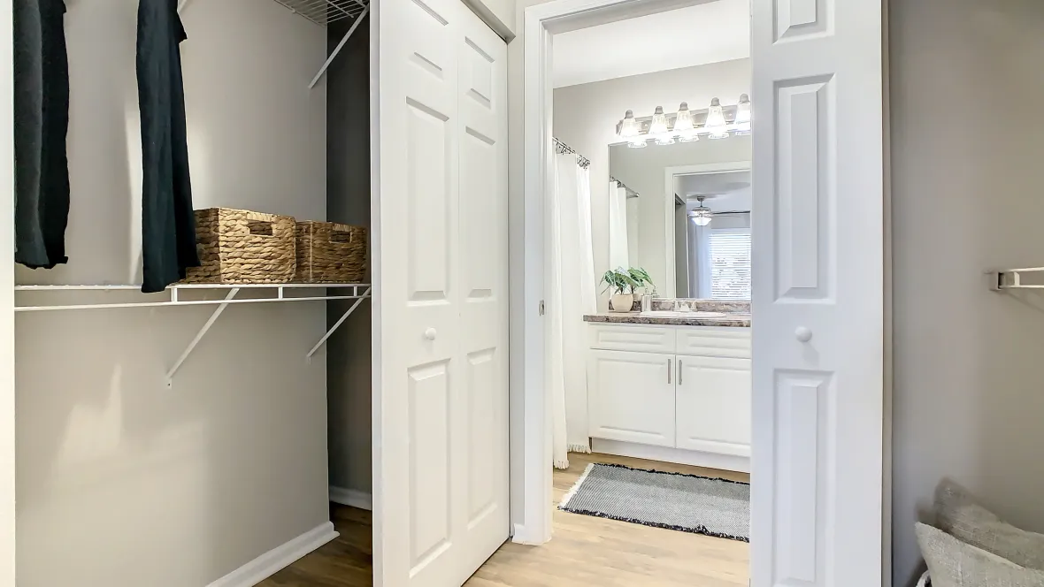 A peek into the lavish master bathroom from a hallway leading from the bedroom reveals closets, with built-in shelfing organizers, on both sides of the hallway, promising practical and abundant storage.