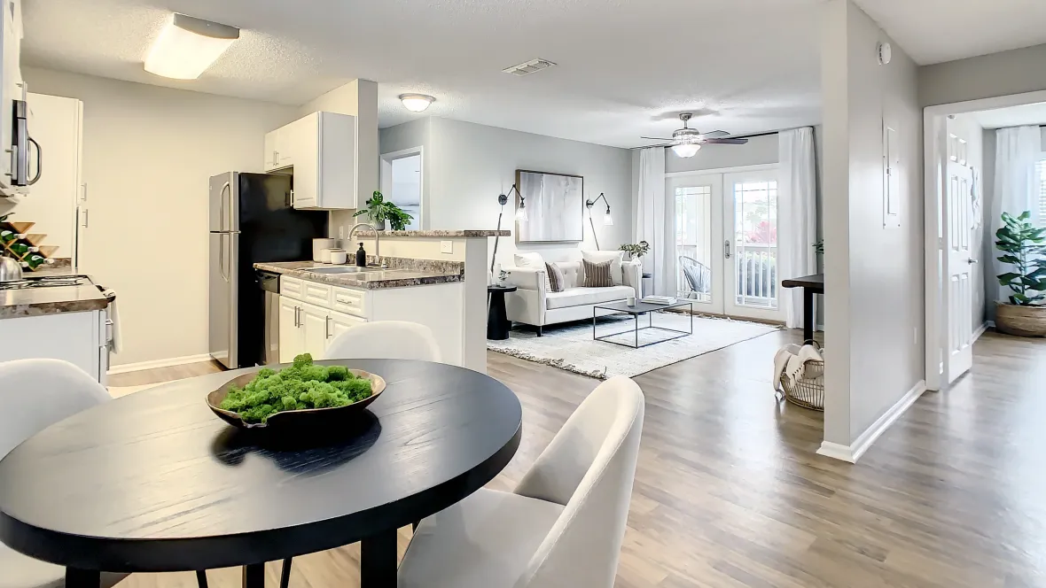 An open floor plan connecting kitchen, dining, and living spaces features chic details like a sleek granite-inspired breakfast bar, wood-style flooring, and ample natural light flooding through the French patio doors.