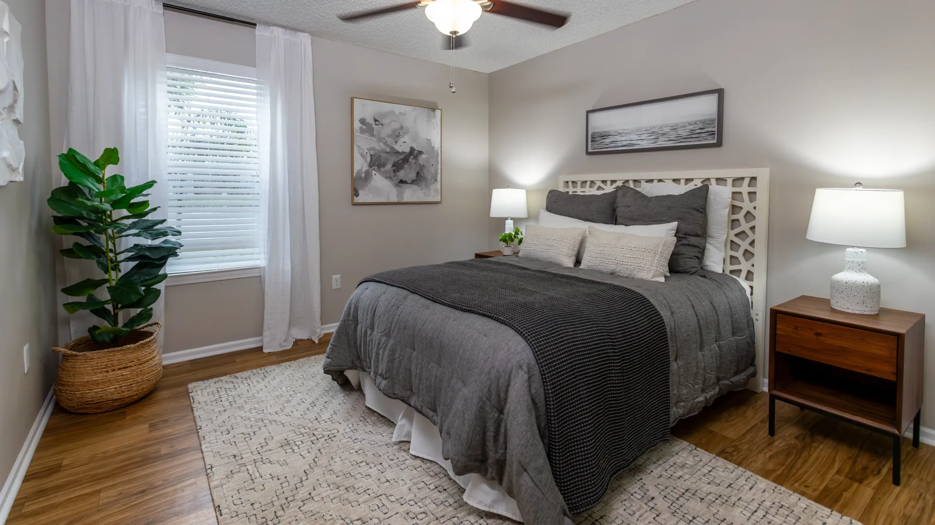 Modern bedroom at Grand Oaks with wood flooring, gray bedding, and natural light.