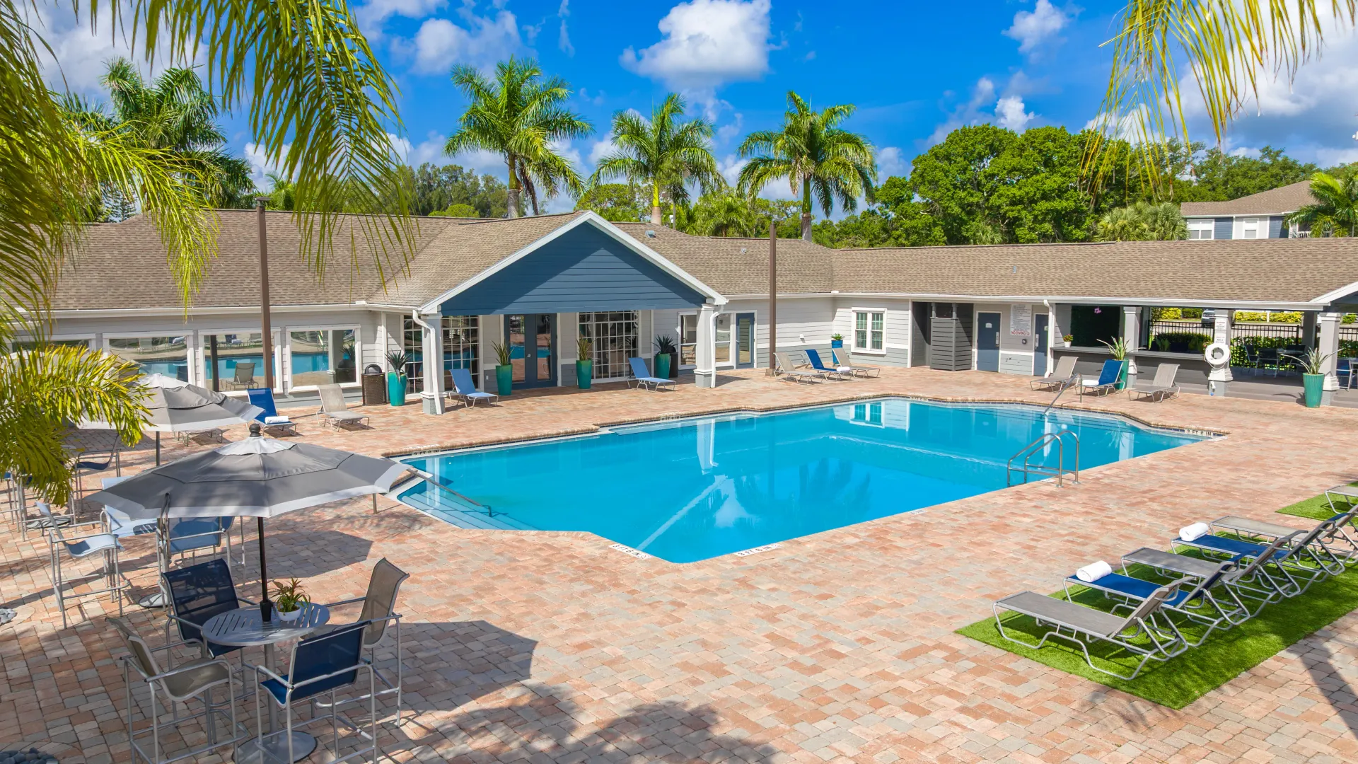Grand Oaks Apartments resort-style pool and expansive sundeck with lounge chairs, umbrellas, and clubhouse in the background.