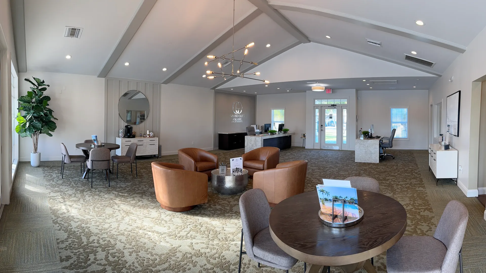 Interior view of Grand Oaks' leasing office featuring modern furniture, a large round table, comfortable chairs, and a reception desk in a spacious, well-lit room.