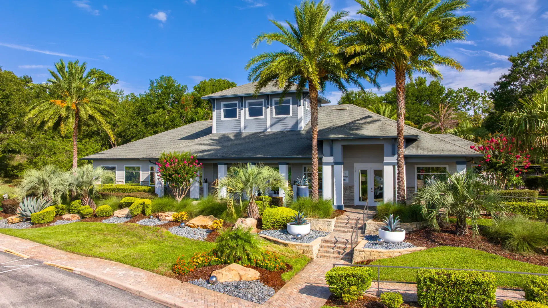 Exterior view of the Elevate 155 clubhouse surrounded by tropical landscaping and palm trees.
