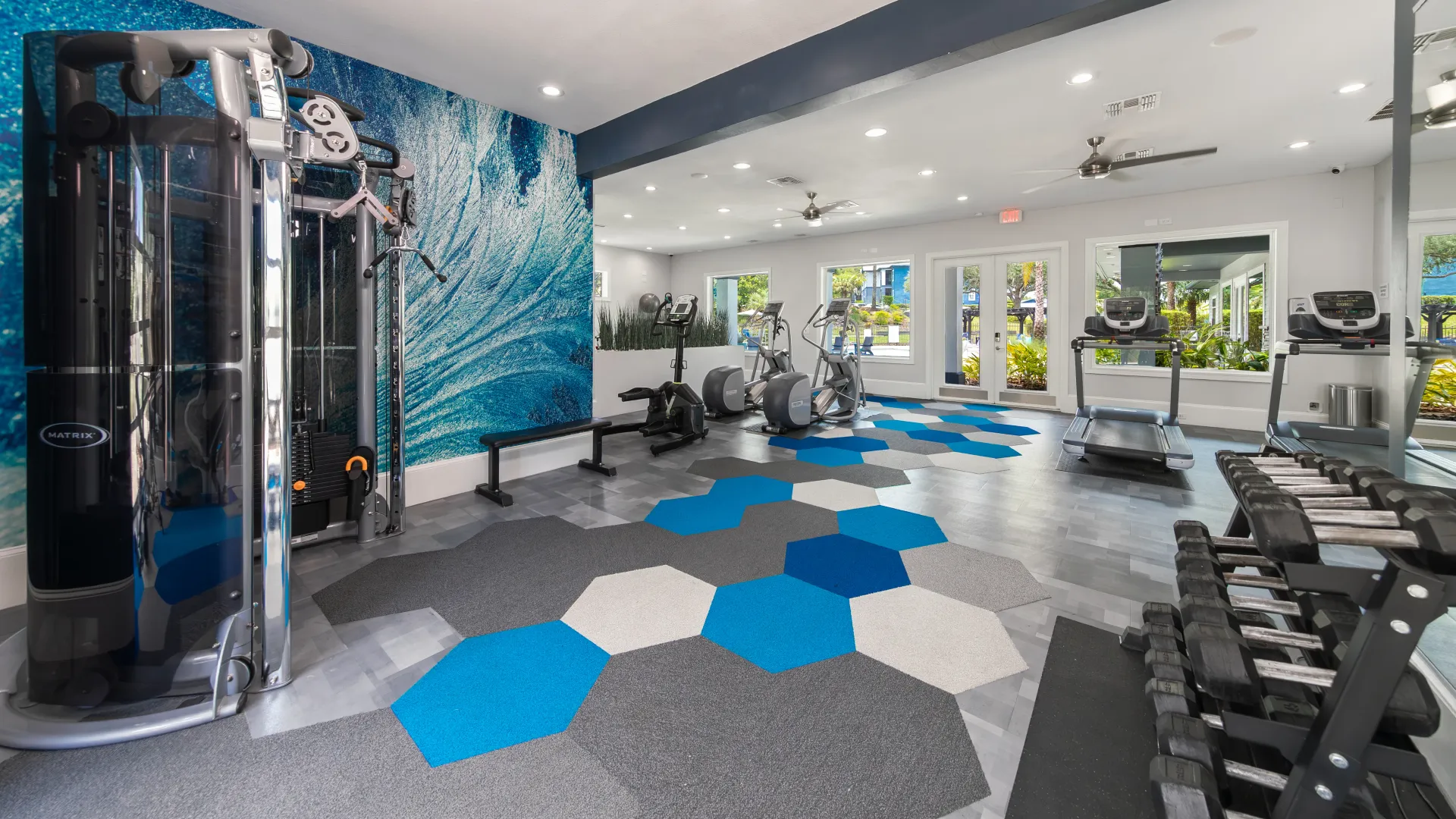 Fitness room with treadmills, ellipticals, dumbbells, and a colorful geometric floor design.