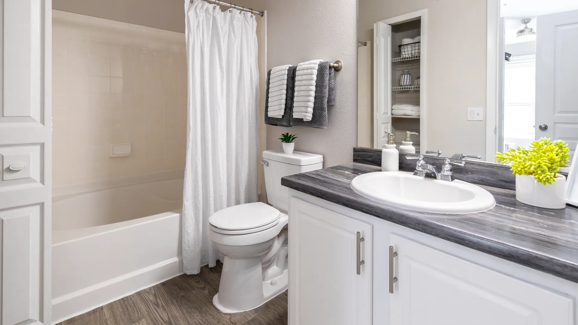 Stylish bathroom with modern vanity, towel rack, toilet, and shower-tub setup at Elevate 155 Apartments.
