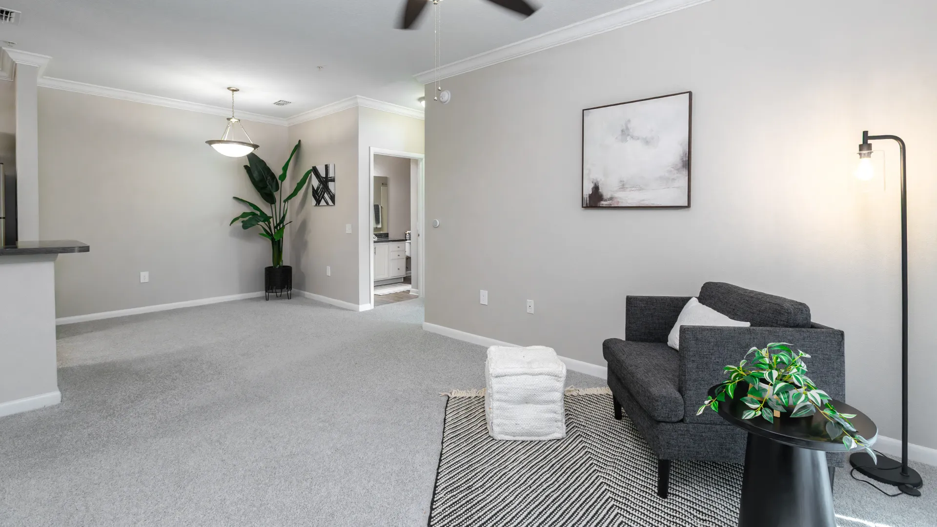 Living room with light gray carpet, neutral walls, ceiling fan, and cozy seating at Elevate 155 Apartments.