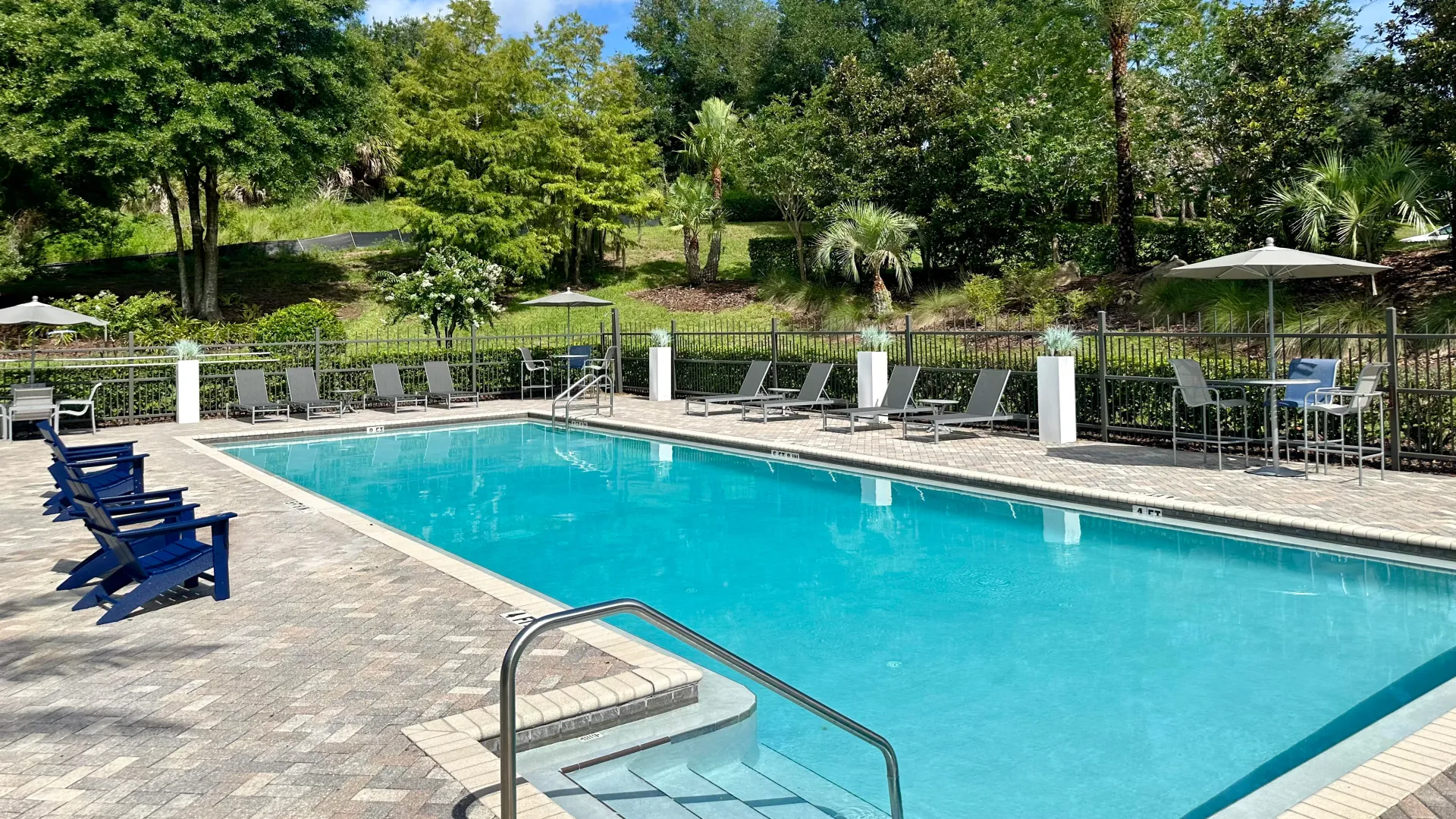 Pool area at Elevate 155 Apartments with lounge chairs, blue Adirondack chairs, and green landscaping.