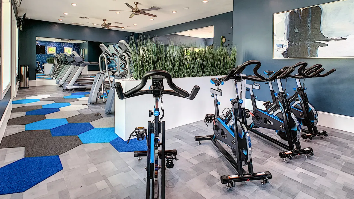 Four exercise bikes with a view of treadmills and ellipticals in the background.