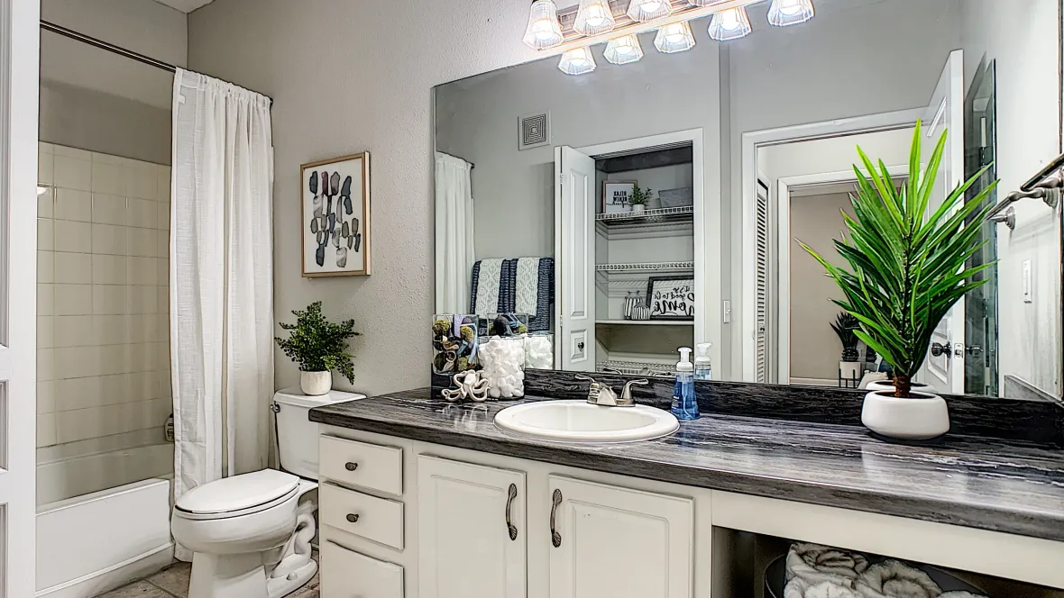 The primary bathroom, featuring an expanded countertop and vanity space, upgraded with white cabinetry, black-fusion countertops, extended mirror, and vanity lighting.