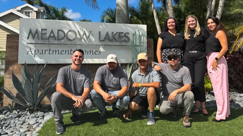 Smiling team members at Meadow Lakes Apartments, standing in front of the community entrance sign.