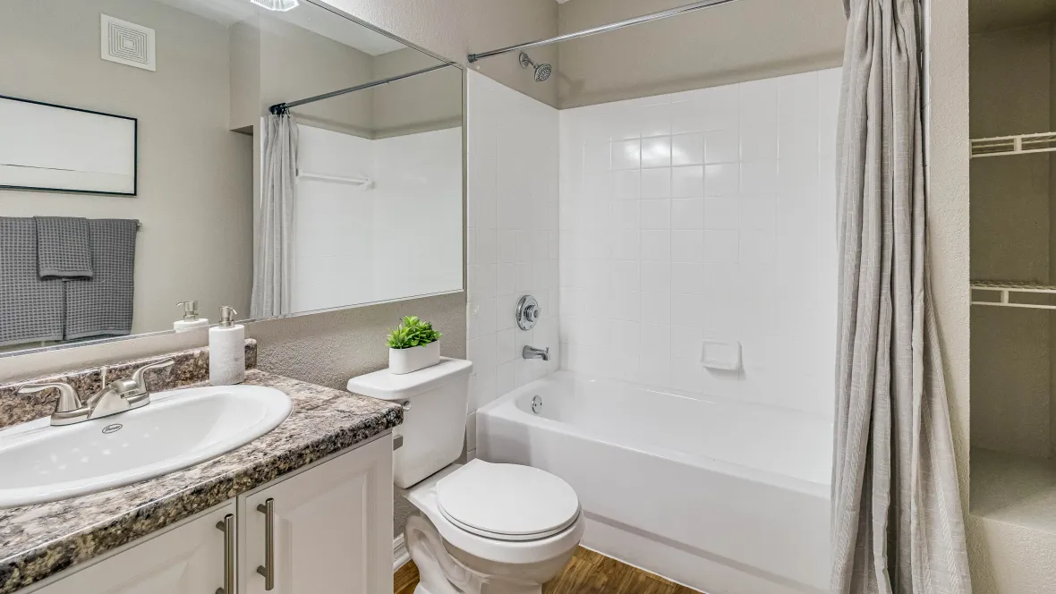 An impressive bathroom a neutral granite-inspired vanity and a white tile shower/tub combo with bright vanity lighting reflecting off the expansive mirror and tub surround.