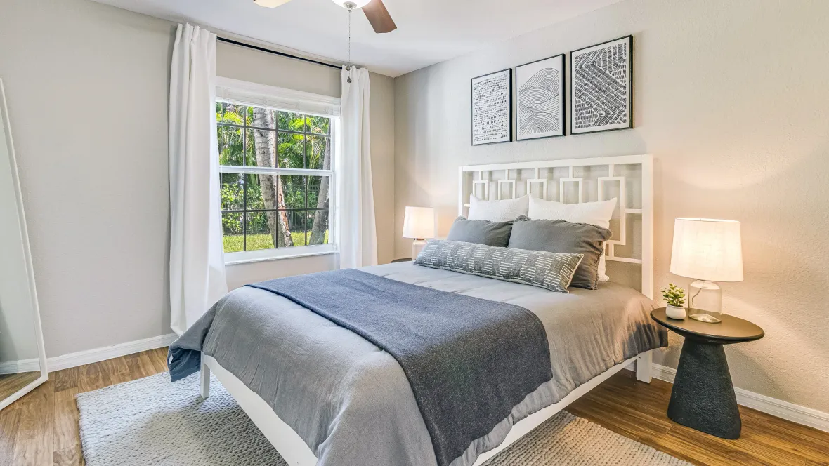 Airy guest bedroom with wood-style flooring, suitable for a king-sized bed, an overhead ceiling fan, and a wide window allowing plentiful natural lighting. 