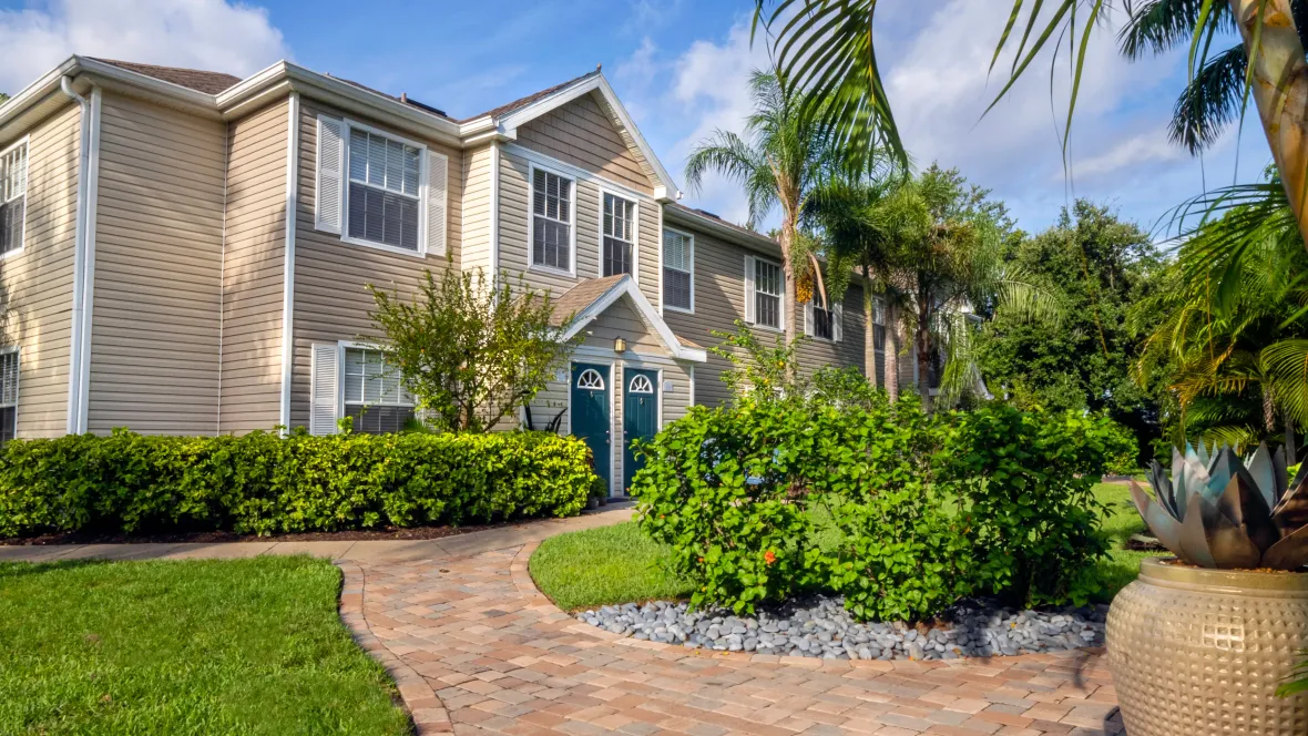 A winding paved path around meticulously cared-for landscaping leading to an apartment building.