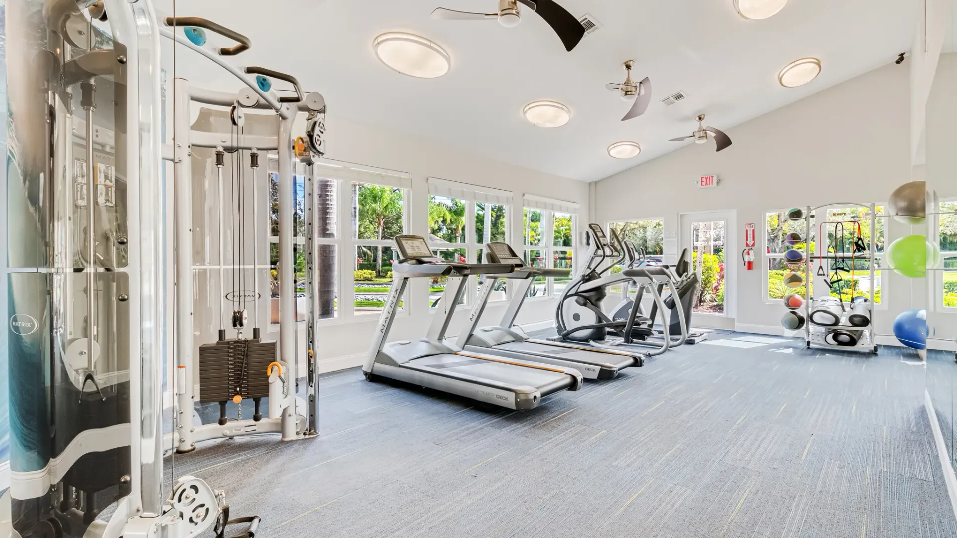 Spacious fitness center featuring cardio machines, weight stations, and wellness accessories with large windows providing natural light.