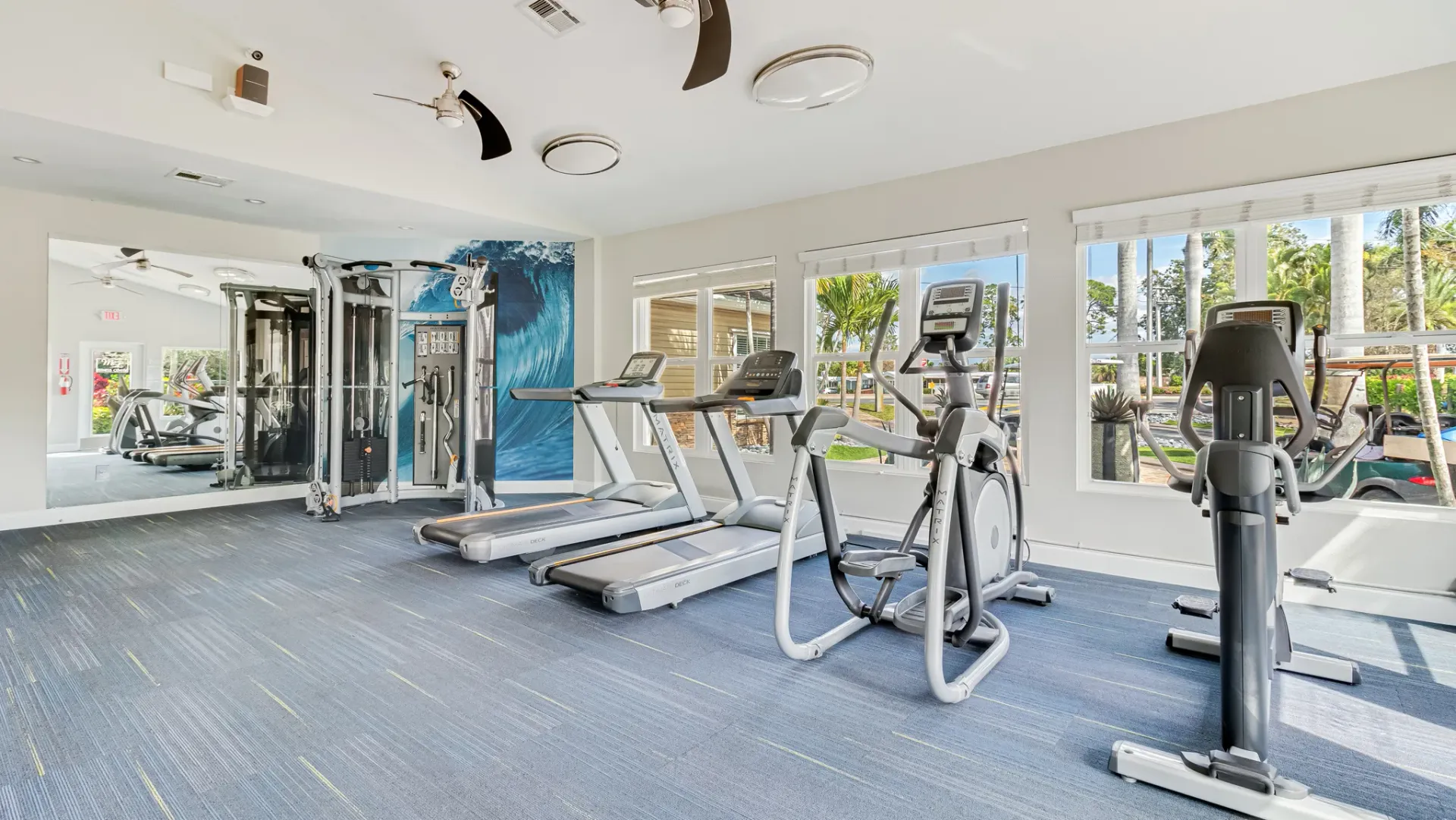 Fitness center with treadmills, ellipticals, and strength training equipment in a spacious room with large windows and a vibrant wall mural.