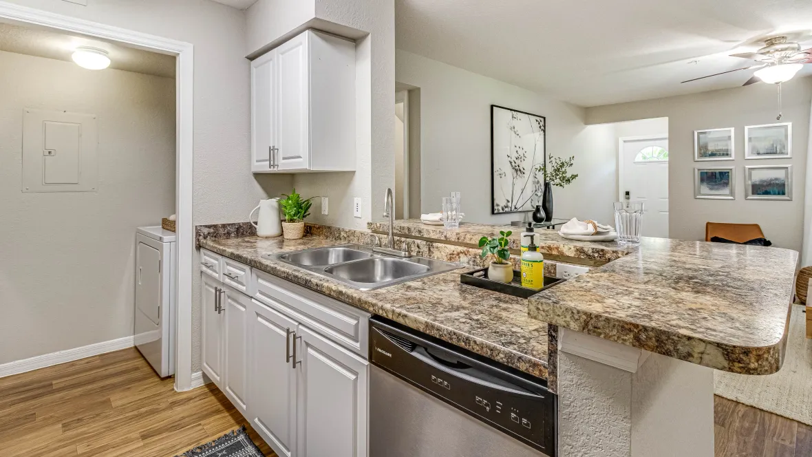 A kitchen with a double sink and a breakfast bar overlooking the living room with a direct line of sight to the front entry door, fostering a connected living experience.